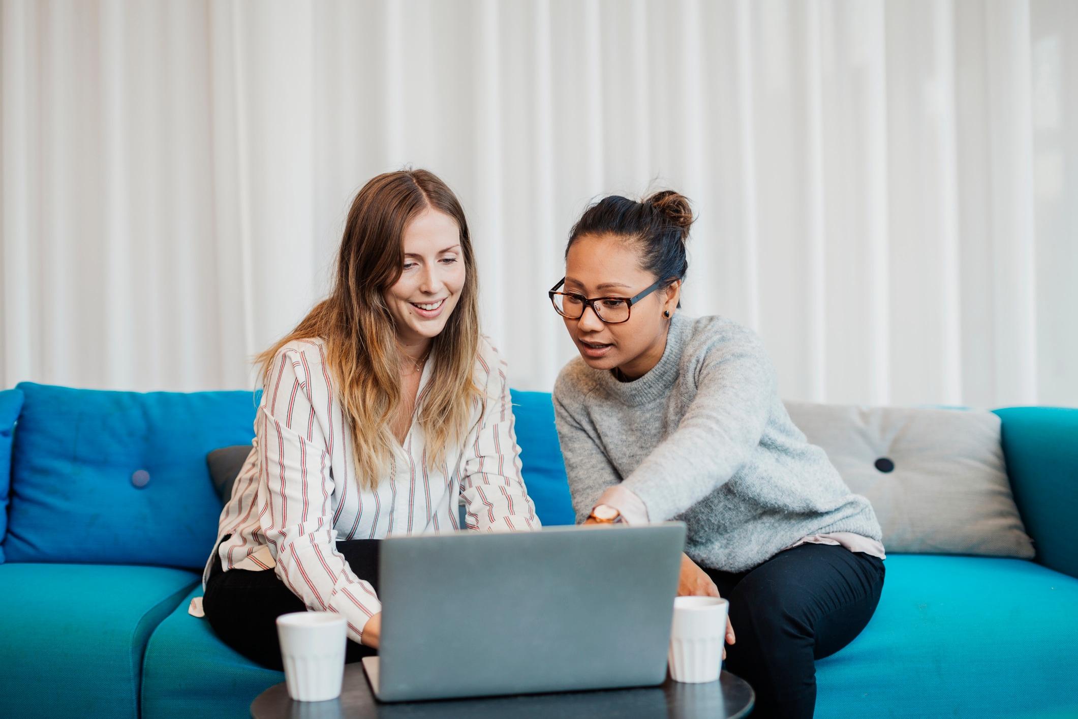 Two women smiling at a laptop. The one on the right points at the screen.