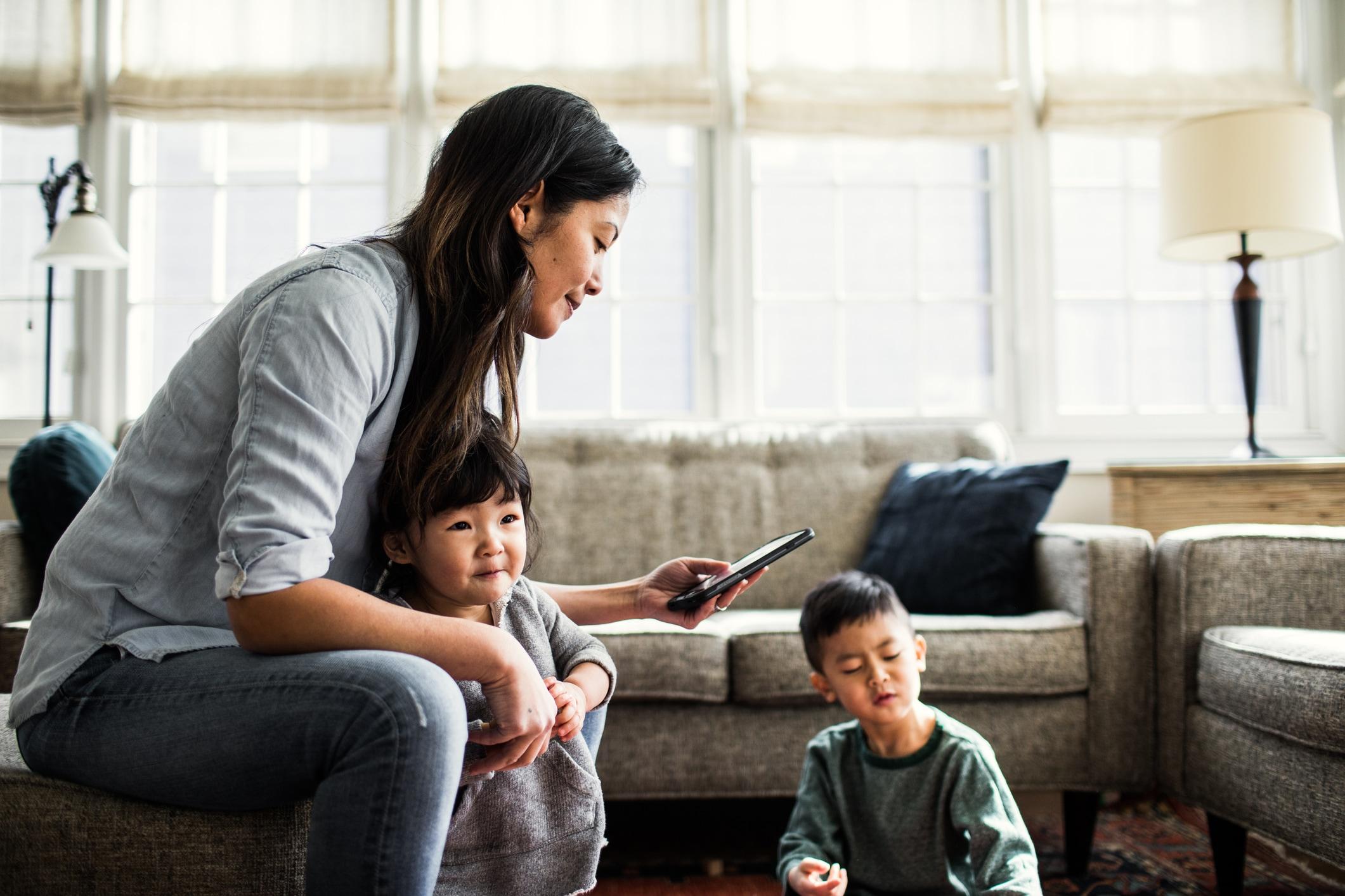 A woman sitting with her two children and smiling at a smartphone.